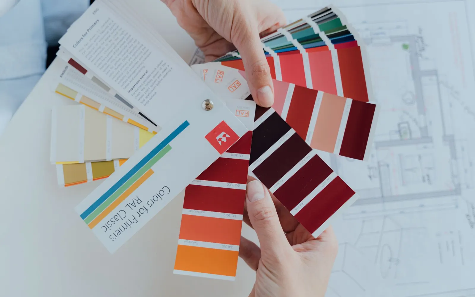 Hands holding fanned color swatch guides over a design plan